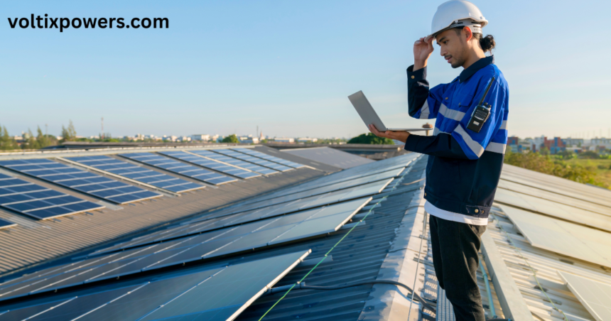 Technician inspecting rooftop solar panels on a large commercial metal roof while using a laptop and wearing a white safety helmet and blue work uniform under a clear blue sky. The image highlights professional solar panel inspection, maintenance, and renewable energy installation. The website name "voltixpowers.com" appears in the top-left corner.